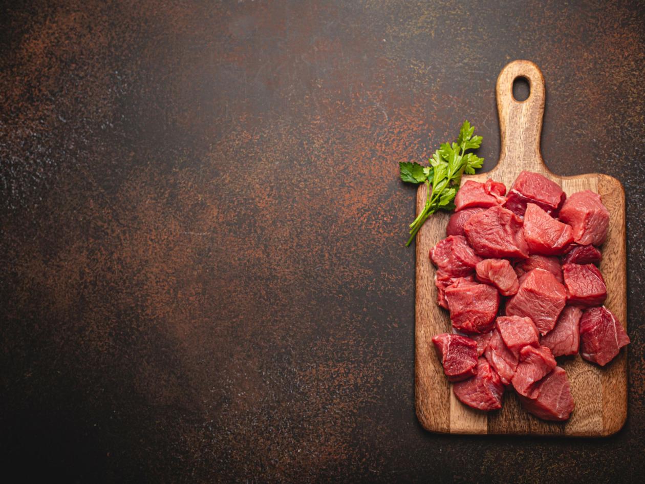Raw Beef Meat Chopped In Cubes With Bunch Of Fresh Parsley On Wooden Cutting Board For Cooking Stew