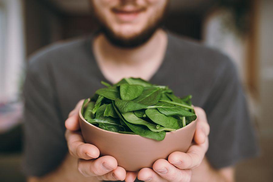 Hands Of Man Holding Fresh Green Salad Leaves Of Spinach On Blurred Background. Healthy Vegetarian E