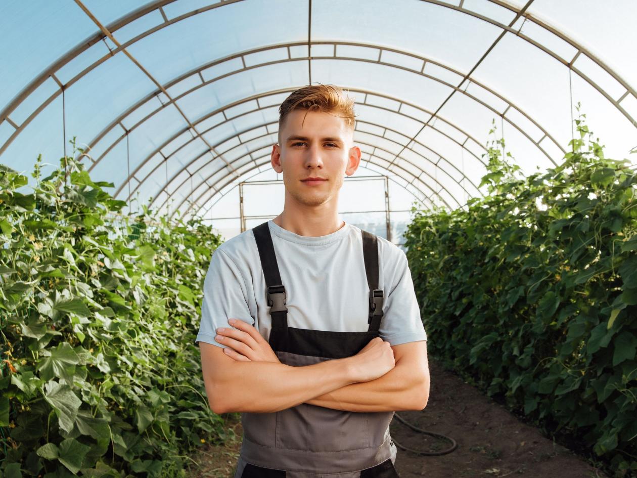 Portrait Of A Young Male Farmer In Overalls In A Greenhouse
