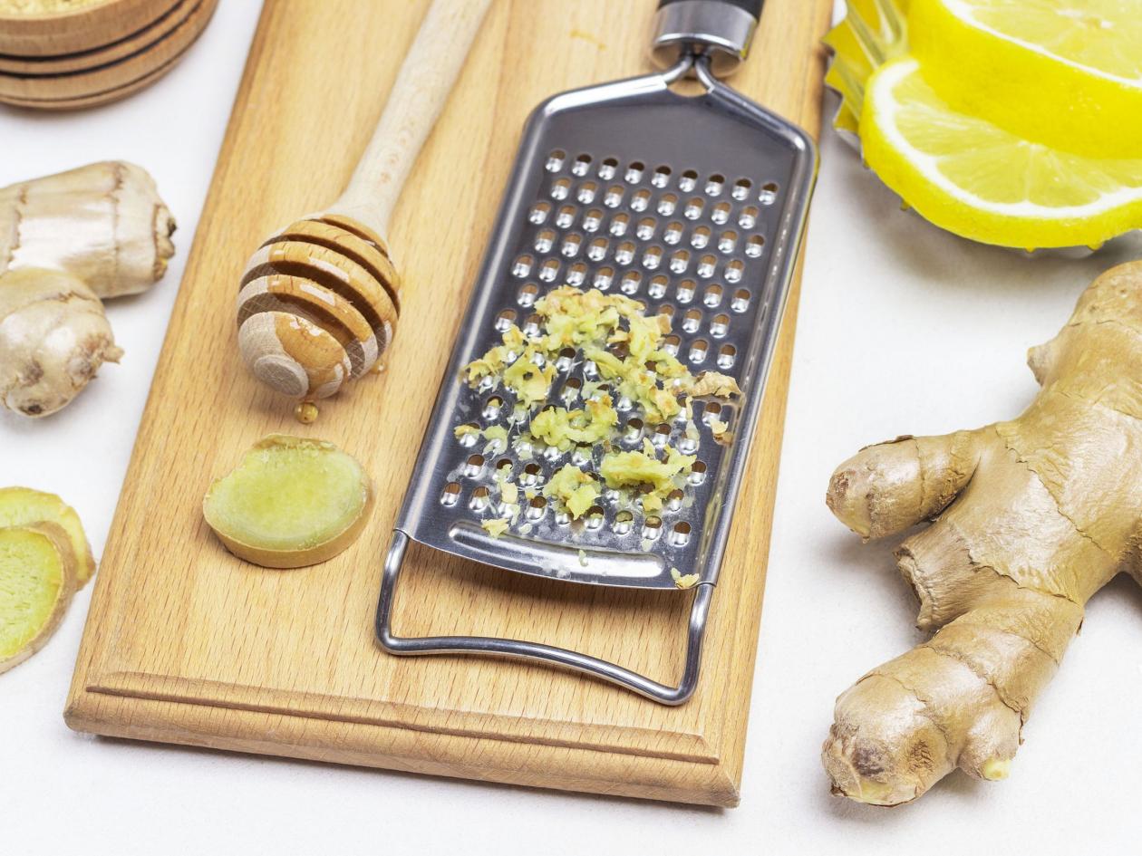 Grater With Grated Ginger. Stick With Honey On Board. Ginger Root And Lemon On Table. White Backgrou