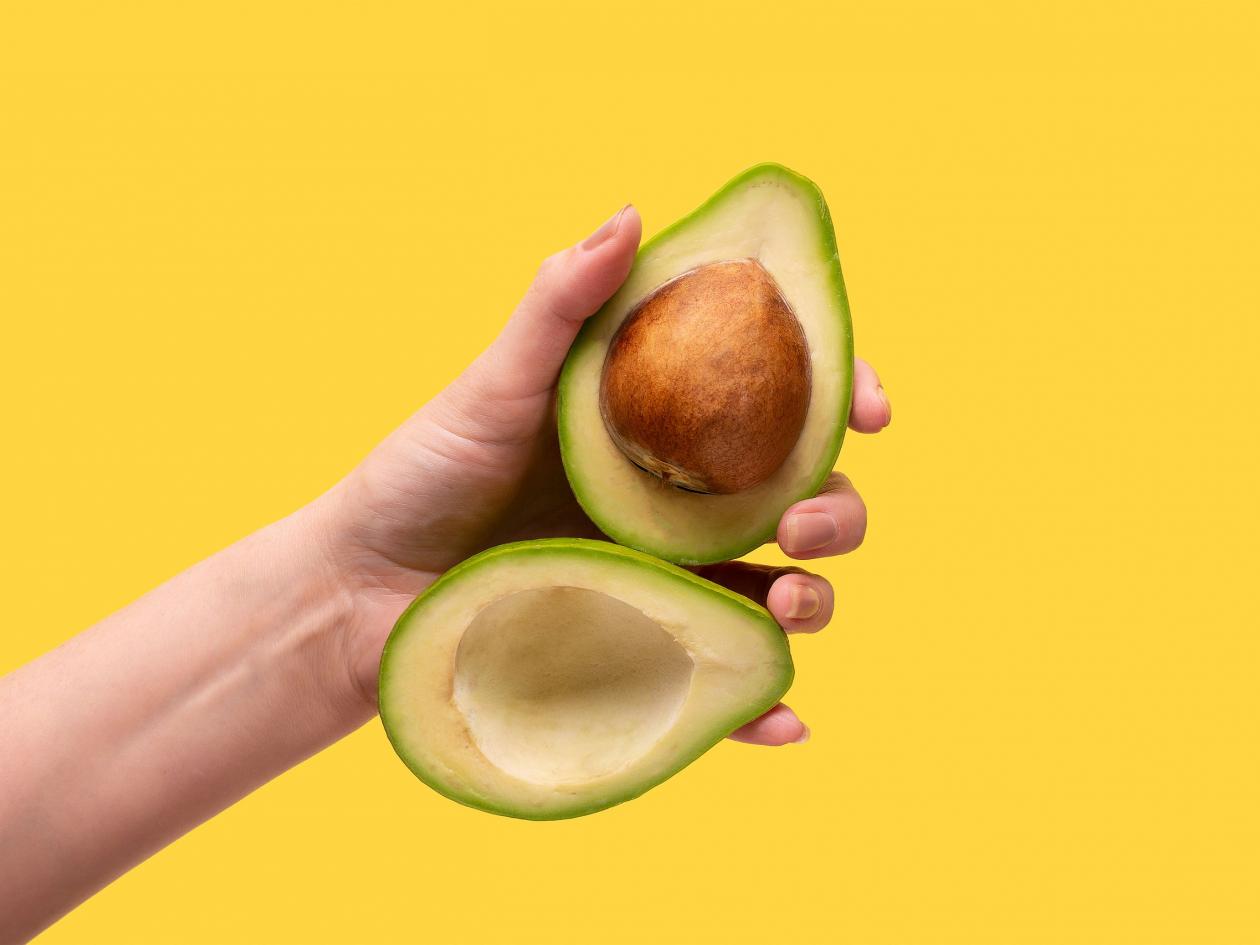 Ripe Avocado Fruit In The Hand Of A Young Girl. Sliced Avocado In Hand.