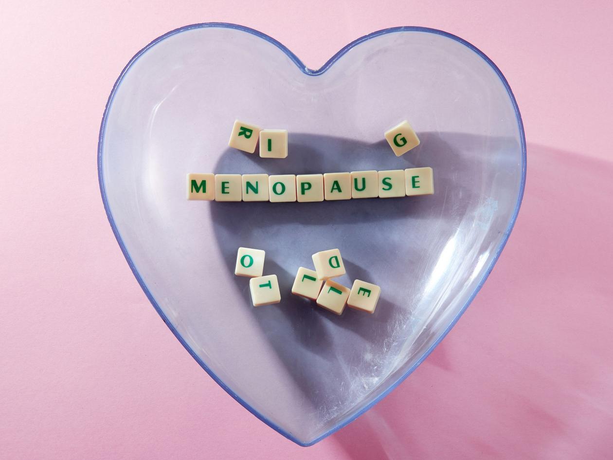 menopause word written on square block in a heart shape container. menopause text on pink backgroun