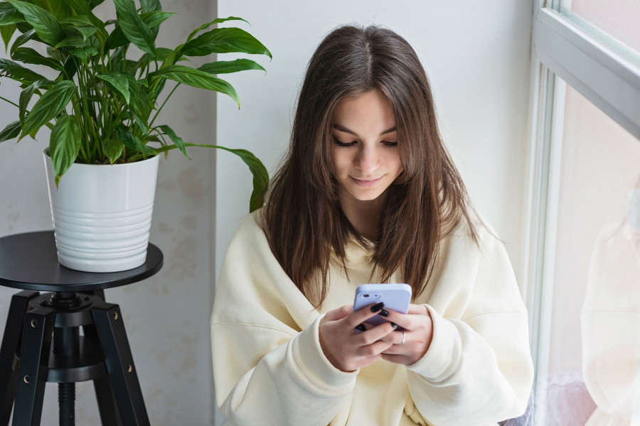 Happy Teenage Girl Looking At Smartphone, Relaxing At Home, Enjoy Using Mobile Online Apps, Playing