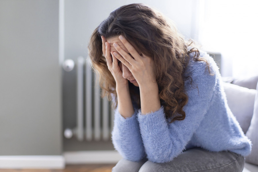 Young Depressed Woman Sitting On Sofa In Living Room. She Feeling Sad And Worried Suffering Depressi